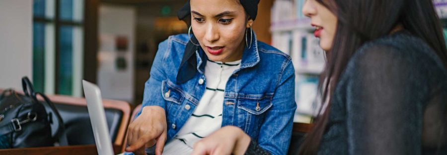 Two women sitting at a table looking at a laptop.