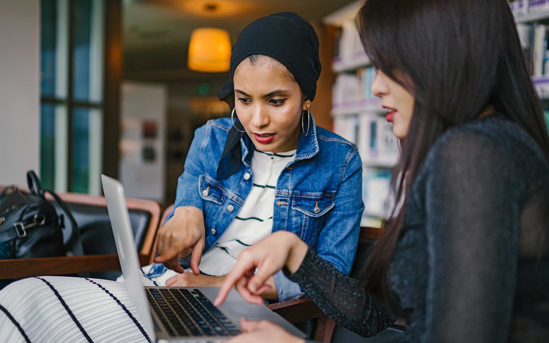 Two women sitting at a table looking at a laptop.