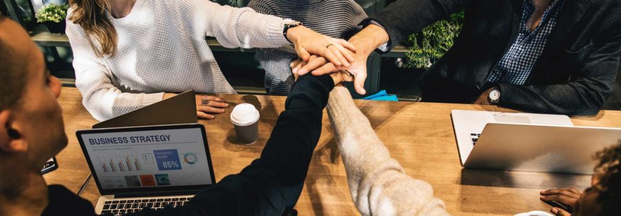 A group of people sitting at a table with their hands together.