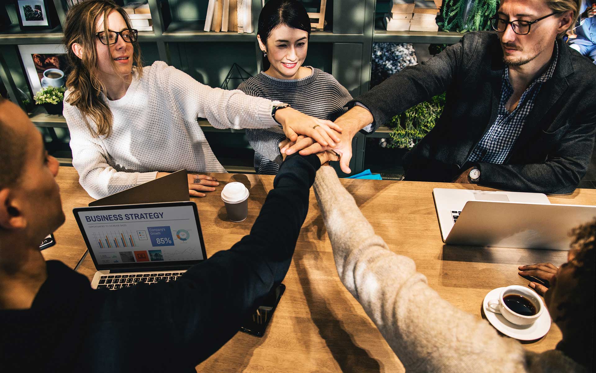 A group of people sitting at a table with their hands together.