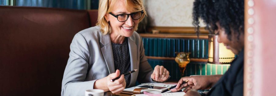 Two women sitting at a table with papers and coffee.