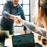 Two people shaking hands over a laptop